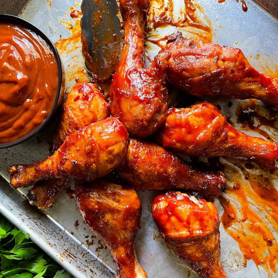 Barbecue chicken legs on a baking sheet with a black bowl full of barbecue sauce.