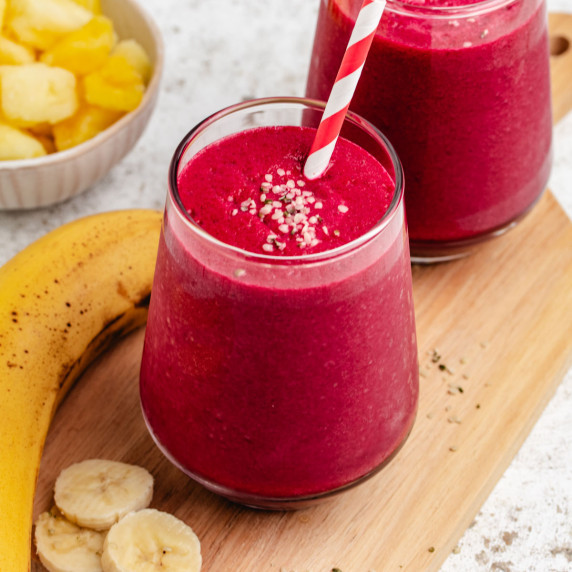 A banana and beetroot smoothie in a glass with a straw and hemp seeds.
