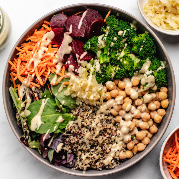 A beet Buddha bowl with chickpeas, broccoli, greens, shredded carrots, beets, and tahini dressing.