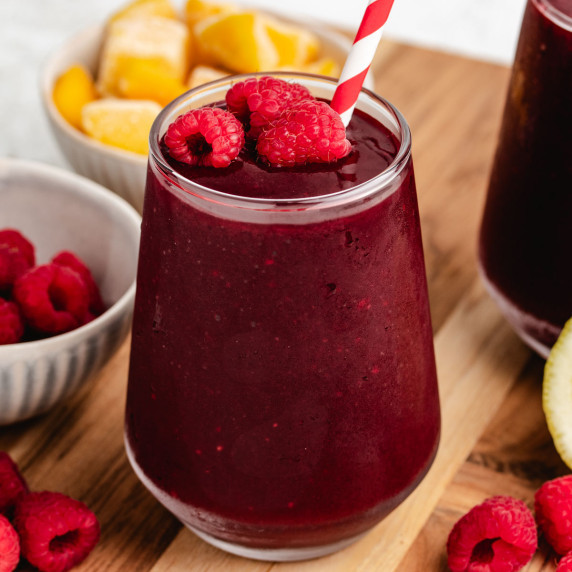 A beet raspberry smoothie in a glass with a straw and fresh raspberries.
