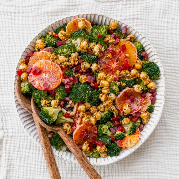 Beetroot, broccoli and orange slices arranged in a fluted white bowl with wooden salad servers.