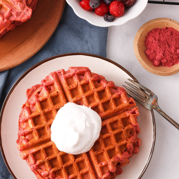 overhead image of beetroot powder waffles with dollop of vegan whipped cream and more toppings
