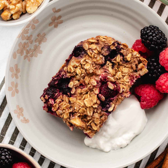 Mixed berry baked oatmeal in a glass dish with a bowl of fresh berries.