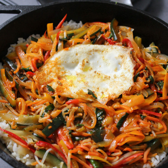 A cast iron pan of Korean bibimbap topped with a fried egg
