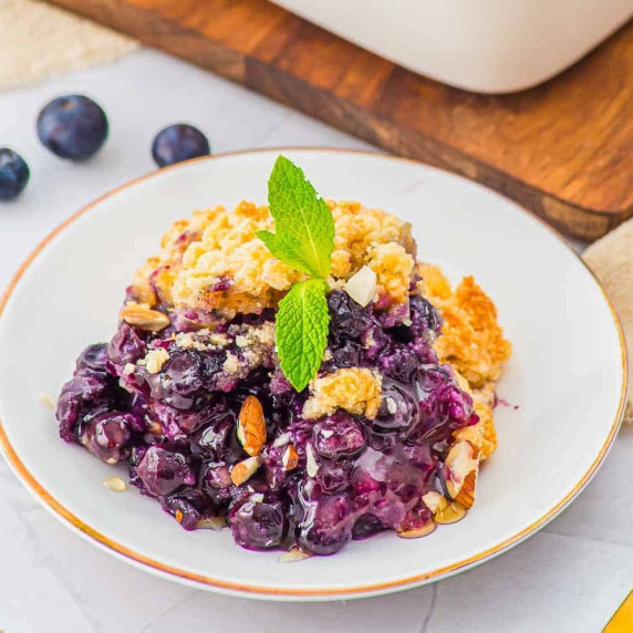 Blueberry cobbler topped with a crumb topping and fresh mint on a dessert plate.