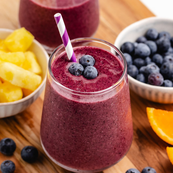 A blueberry pineapple smoothie in a glass with a straw and fresh blueberries on top.
