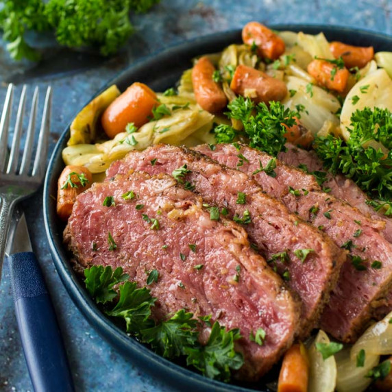 Side close up view of braised corned beef with vegetables garnished with herbs on a black plate with