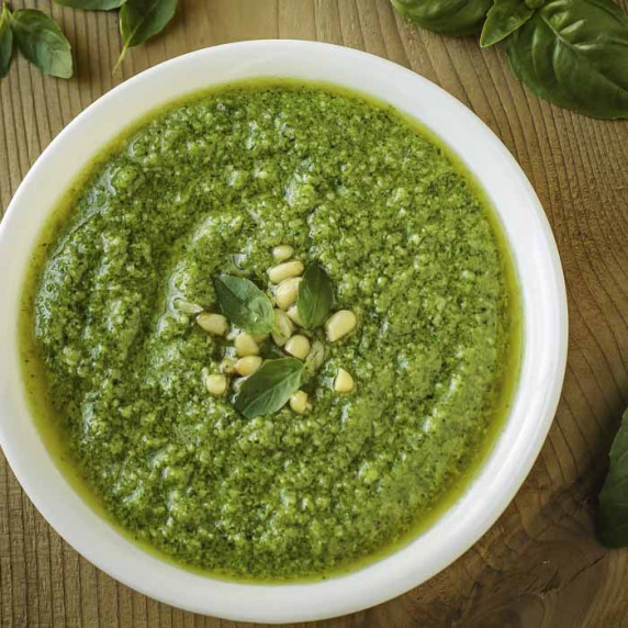 Overhead shot of broccoli pesto in a white bowl garnished with basil and pine nuts.