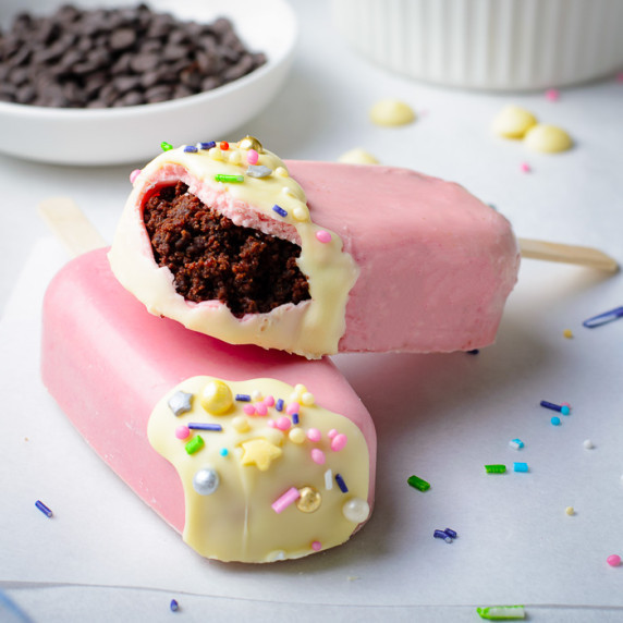 Side shot of two cakesicles stacked on each other, with a bite taken out of the top on and sprinkles