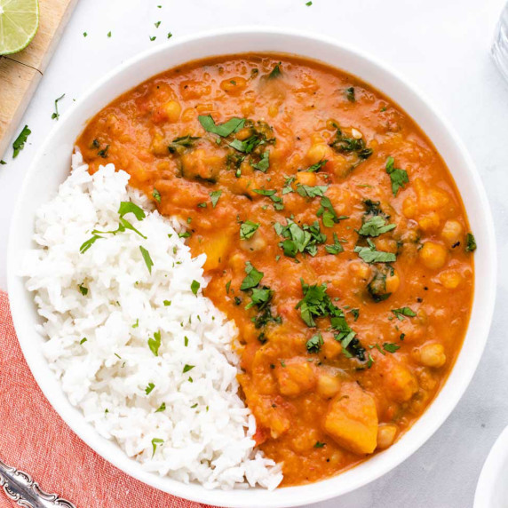 Butternut squash chickpea curry in a bowl with white rice and chopped cilantro.