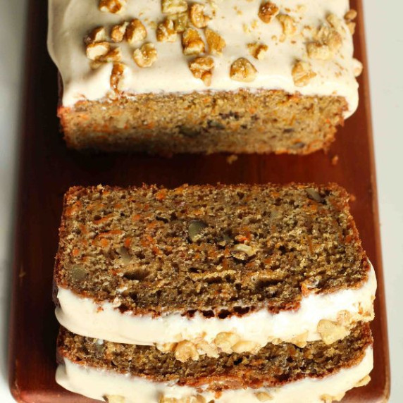 A slice of carrot cake loaf with frosting and nuts on a white plate with a fork.