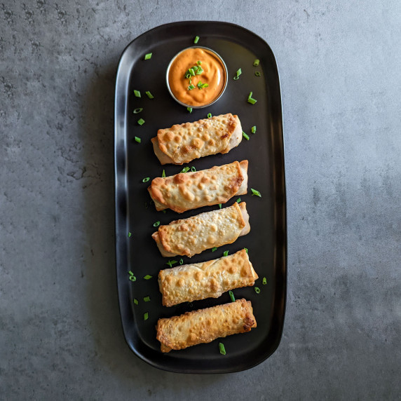 A long serving tray of crispy cheeseburger egg rolls with spicy sriracha mayo dipping sauce