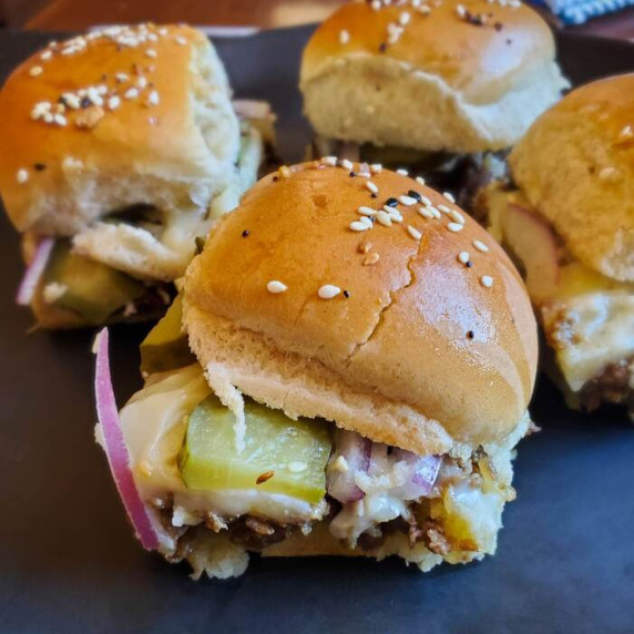 Golden brown toasted bun, slice of green pickle and purple red onions against a black cutting board.