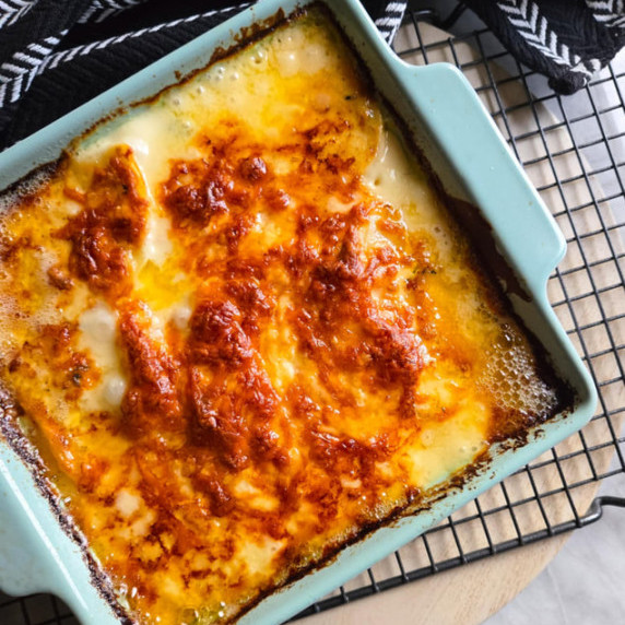 A blue baking dish full of golden brown, creamy scalloped potatoes.