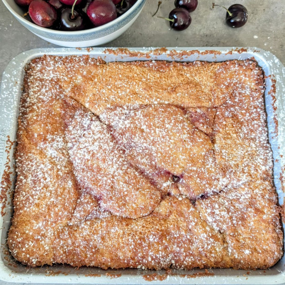 A pan of cherry butter cake topped with a sprinkle of powdered sugar.