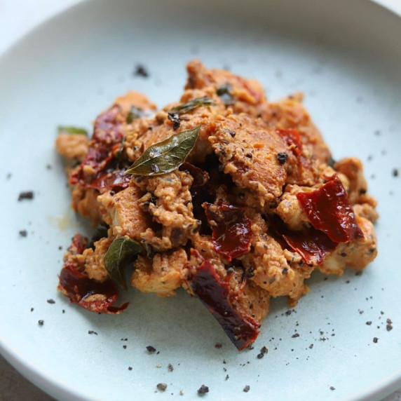 A serving of chicken 65 on a blue plate with crushed black pepper.