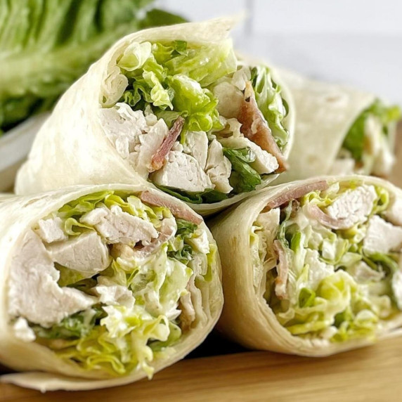Chicken caesar salad wrapped in tortillas on a wooden board with lettuce.