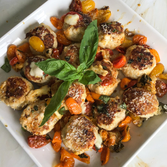 Ground chicken meatballs seared in a pan with blistered tomatoes and topped with burrata and basil