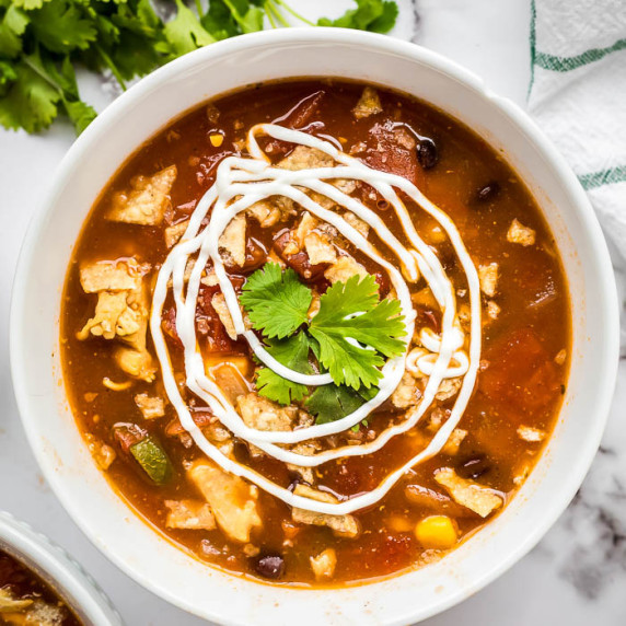 Overhead shot of chicken tortilla soup in a white bowl garnished with swirls of sour cream and herbs