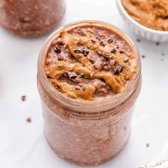 Chocolate peanut butter overnight oats in a jar with peanut butter drizzled on top.