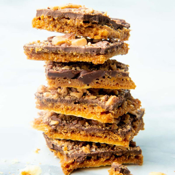Pieces of Saltine Cracker Toffee stacked up high on a white background.