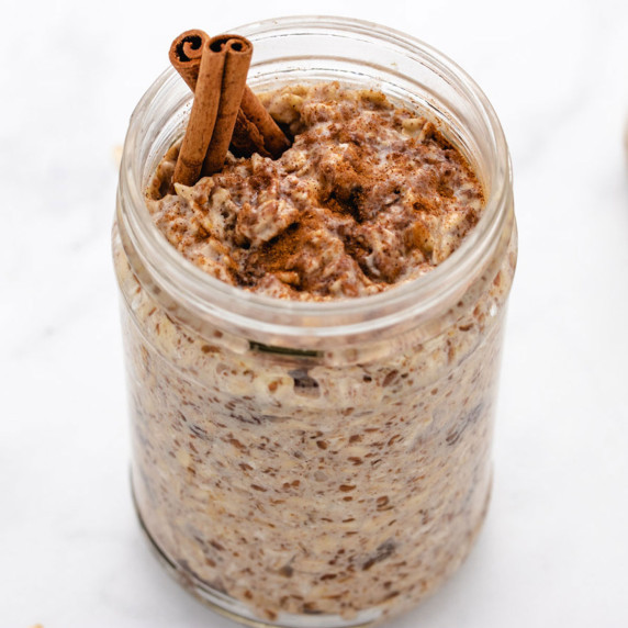 Cinnamon overnight oats in a glass jar with cinnamon sticks.