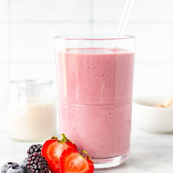 Mixed berry smoothie on a counter with fresh strawberries, blackberries, and blueberries beside it.