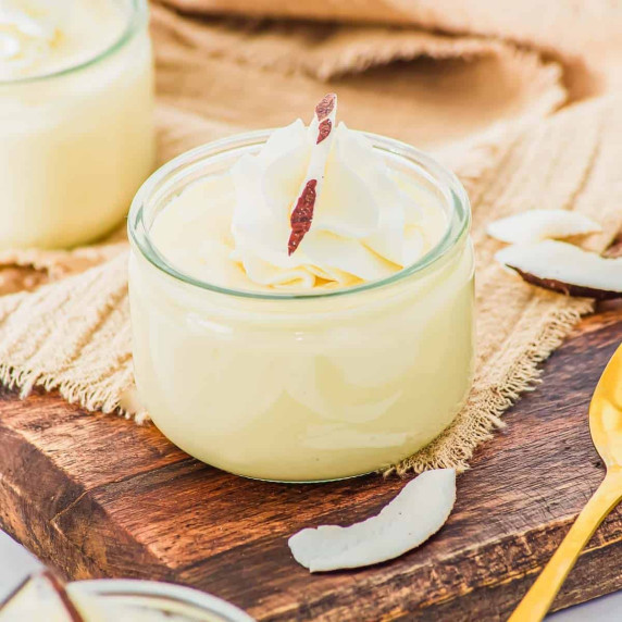 Coconut pudding topped with whipped cream in a glass jar on a wooden board.