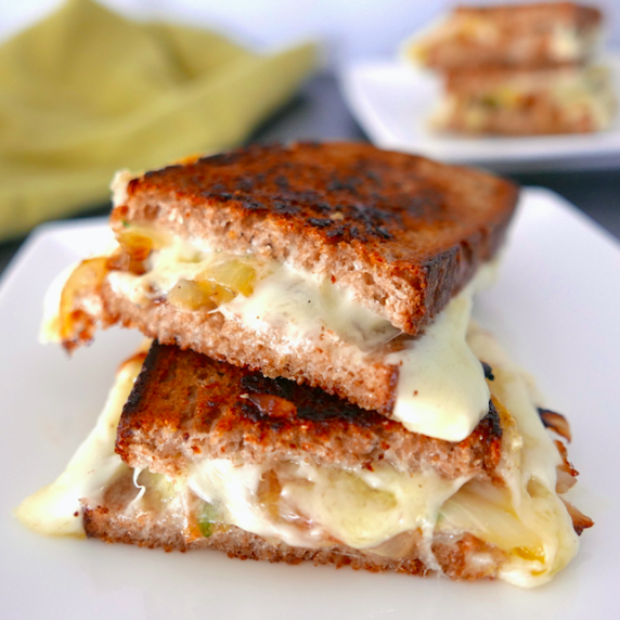 french onion grilled cheese cut in half and stacked on top of each other sitting on a white plate