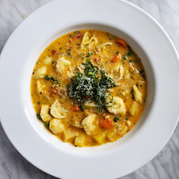 White rimmed bowl with tortellini chowder against a marble backdrop. 