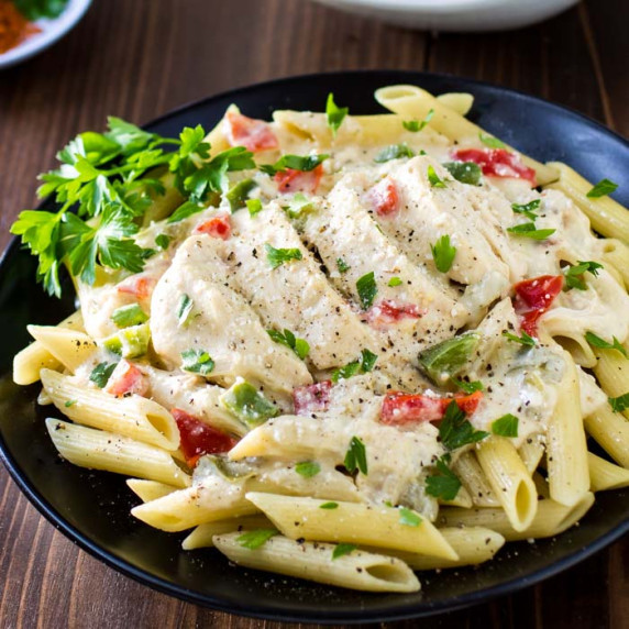 Close up shot of creamy cayenne chicken on a black plate with herbs sprinkled.