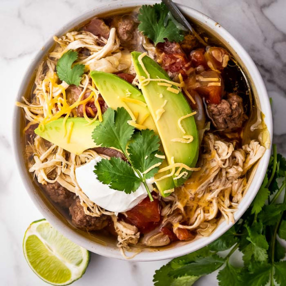 Overhead shot of chicken taco soup with slices of avocado, fresh cilantro, and shredded cheese.