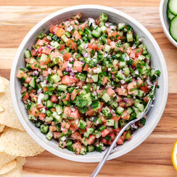 Cucumber pico de gallo mixed in a bowl with a spoon and chips to the side.