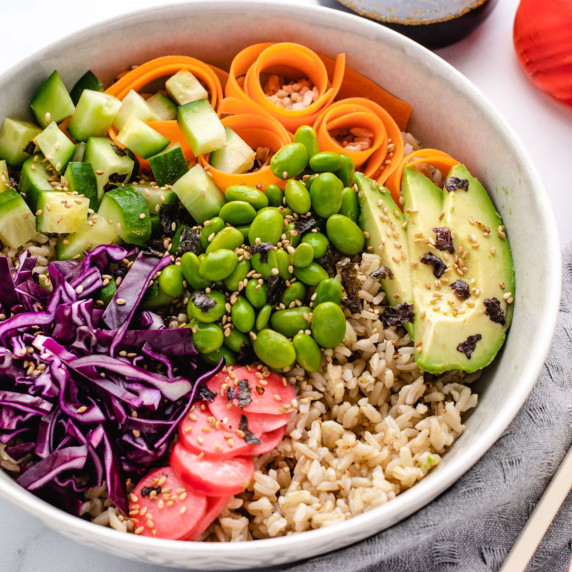 Vegan sushi bowl with rice, cabbage, avocado, cucumber, edamame, and carrots in a bowl.