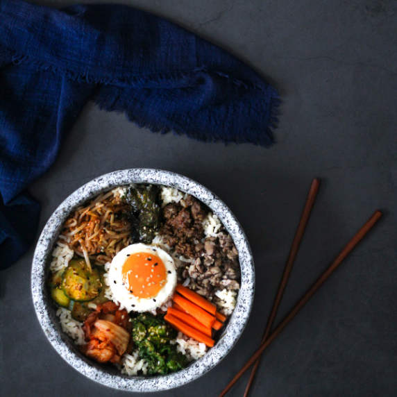 Bibimbap in a dolsot (stone bowl) with brown chop sticks on a gray surface.