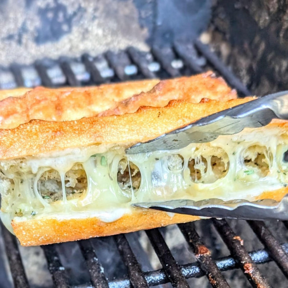 Cheesy garlic bread on a grill being opened slightly to check that the cheese is fully melted