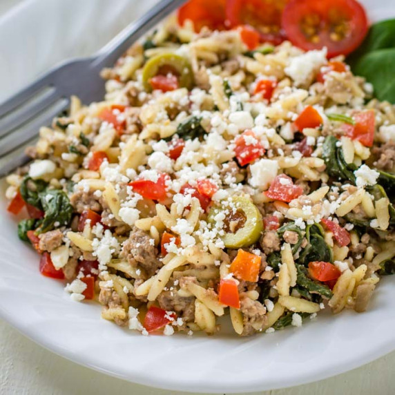 Side shot of beef and orzo skillet meal on a white plate with a fork  on the side. 