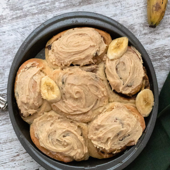 Top view of a round pan of peanut butter iced banana cinnamon rolls on top of a green napkin