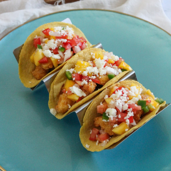 A plate of three fried fish tacos with mango salsa in a taco stand