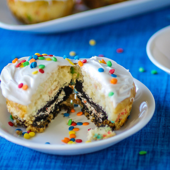 Side close up shot of a cupcake split in half on a small white plate with more cupcakes in the back.