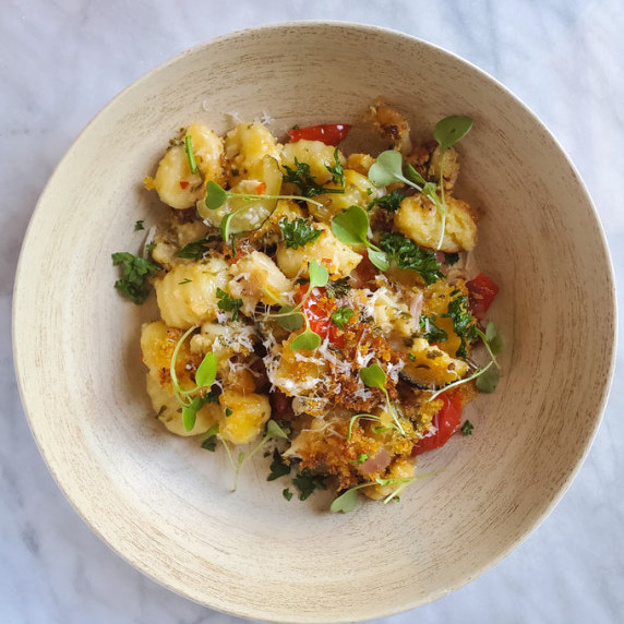 Wooden bowl filled with gnocchi and vegetables against a white marble background.