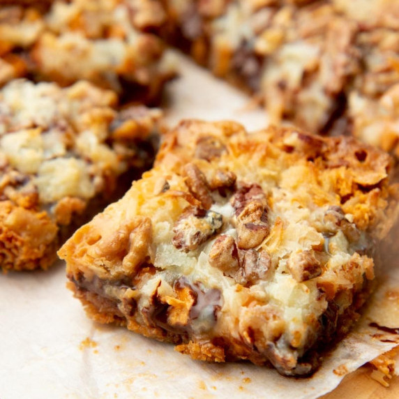 Close up of a 7 layer magic cookie bar cut into a square on parchment paper.