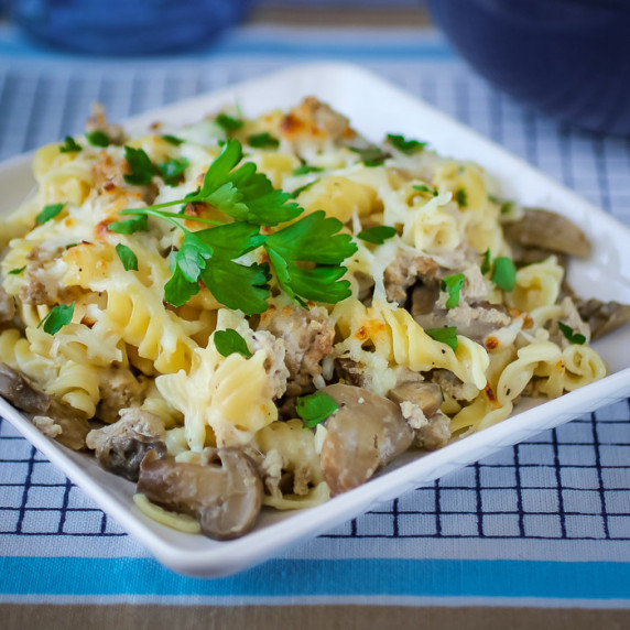 Angled overhead view of turkey Alfredo garnished with herbs on a white square plate on a blue mat.
