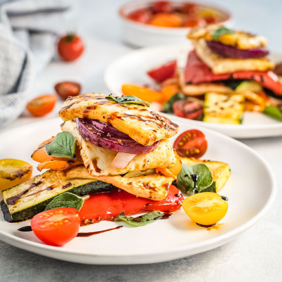Side view of two white plates of colorful halloumi salad garnished with herbs on a white surface.