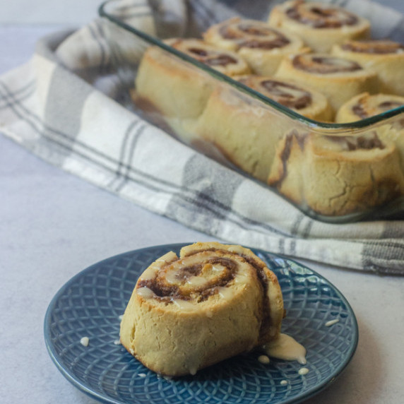 cinnamon roll sitting on a blue plate with more cinnamon rolls in clear dish in the background