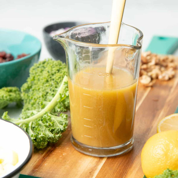 A glass measuring cup with homemade honey mustard dressing stands with a spoon in it on a counter.