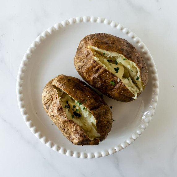 two baked potatoes on a white plate sliced with a pat of butter.