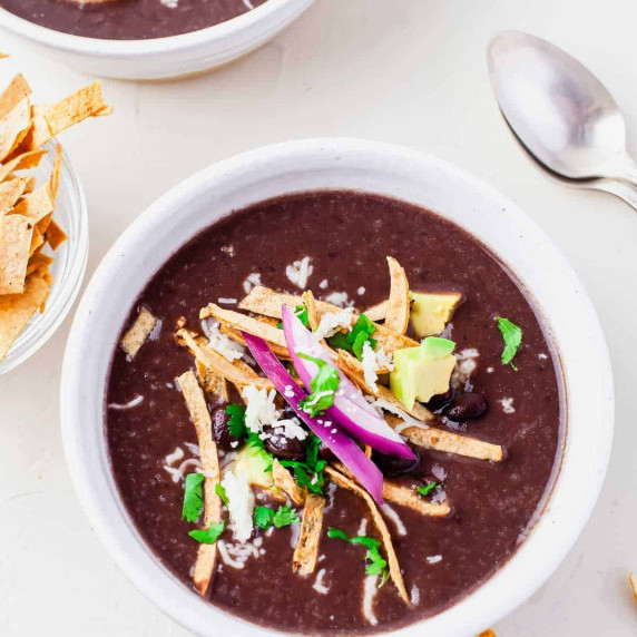 Bowl of black bean soup topped with tortilla strips and avocado