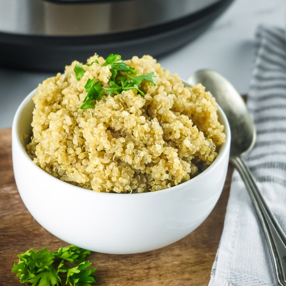 Side shot of a white bowl of fluffy quinoa garnished with fresh herbs on a wooden surface.