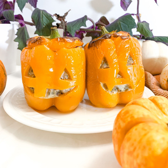 two orange jack o'lantern stuffed peppers on a white plate with a purple passion vine behind